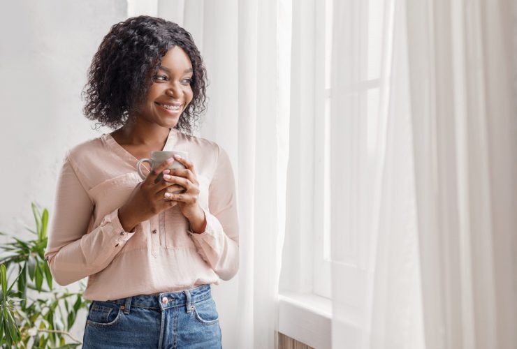 woman next to curtains drinking cofee