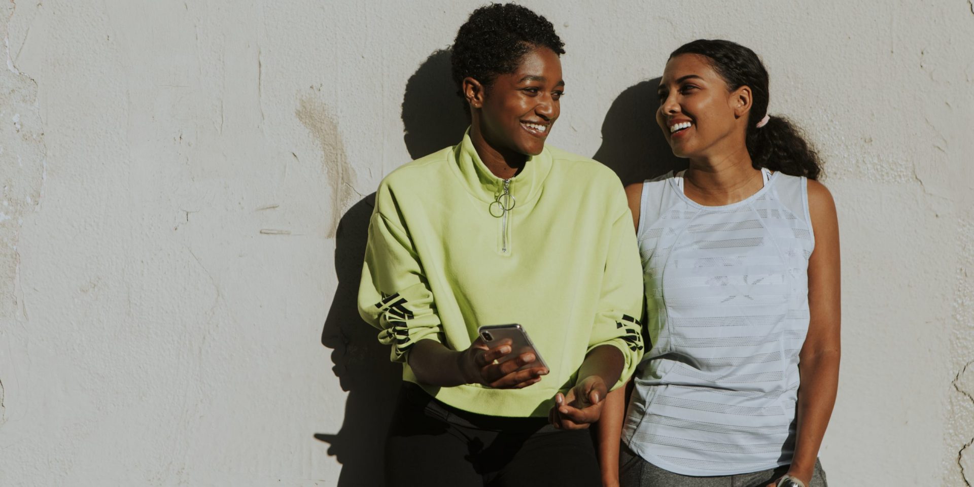 Two women in the sun against a white wall